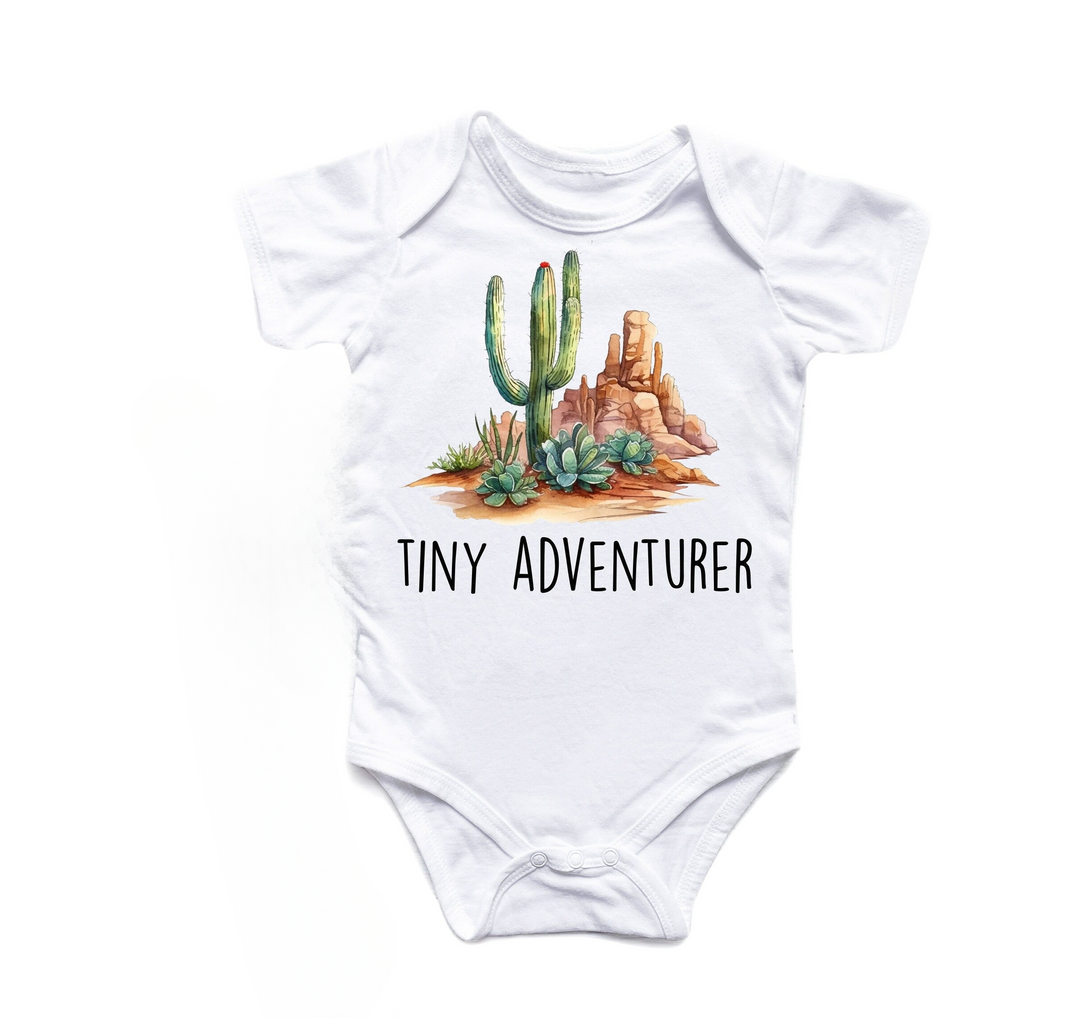 a white baby bodysuit with a cactus and rocks on it that says tiny adventurer